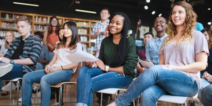 A diverse group of young adults in a classroom, smiling and engaging in a class. Students of various ethnicities and genders studying together in a class. Education and knowledge.
