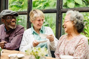 Three diverse elderly friends enjoying tea and laughter at the table. Smiling elderly group, diverse elderly gathering, elderly joy, elderly friendship. Happy seniors have a good time with friends