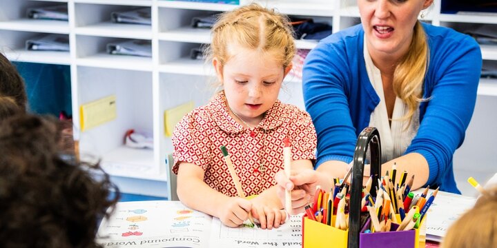 A young child drawing with a teacher in a classroom. The teacher assists the child with drawing. Classroom with colorful supplies and engaged learning. Teacher working with elementary school children.