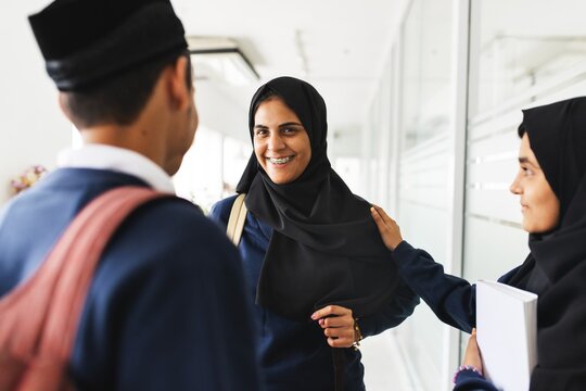 Group of people talking, smiling, and interacting in a hallway. Muslim student girl smiling while talking with diverse friends. Group of diverse students having a conversation in a bright hallway - Powered by Adobe