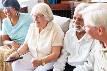 Group of diverse senior friends sitting on a couch, smiling and watching TV together. Diverse senior group enjoying time and companionship together. Senior friendship and retirement life.