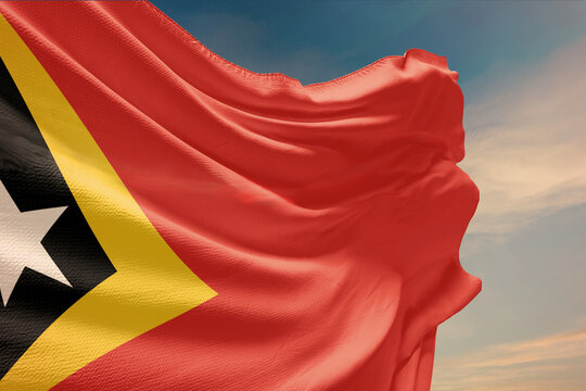Waving flag of East Timor in blue sky. East Timor flag on pole for Independence Day. The symbol of the state on wavy fabric.