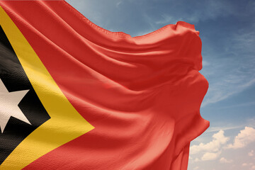 Waving flag of East Timor in blue sky. East Timor flag on pole for Independence Day. The symbol of the state on wavy fabric.