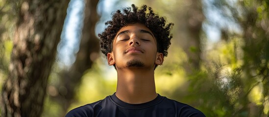 Teenage boy with curly hair meditating outdoors in natural green setting with soft sunlight highlighting his face promoting youth wellness and mindfulness
