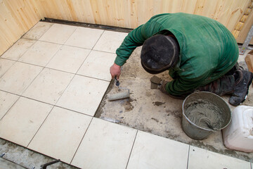 A man is laying down on the floor and painting a tile