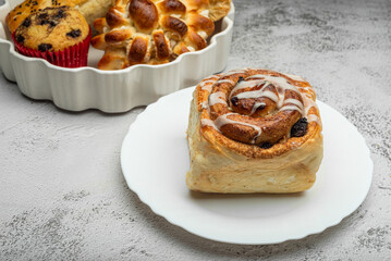 Close-up of a freshly baked cinnamon roll with a generous swirl of icing, on a white plate