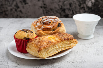 Close-up of a white plate with different freshly baked desserts, cinnamon roll, cupcake, and a sweet pastry.