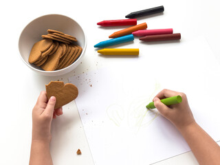 Child drawing with crayons while holding heart shaped cookie