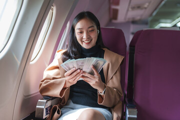 Fototapeta premium Happy businesswoman counting dollar banknotes while traveling by airplane, relishing financial success and the rewards of a productive business trip, radiating joy and accomplishment