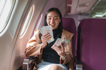 Excited businesswoman counting her earnings in us dollar bills while traveling on an airplane, enjoying her financial success during a business trip