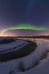 A river at night with a vibrant aurora borealis illuminating the sky and reflecting off its surface.