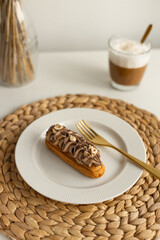 Closeup view hazelnut chocolate eclair on plate with coffee cup