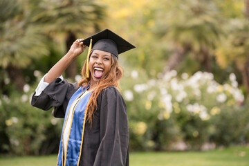Woman graduate laughing with cap and gown holding her cap