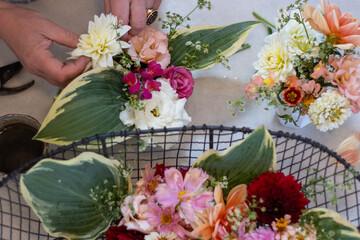 Person arranging various colorful flowers and greenery in vases