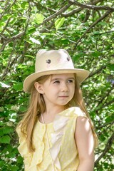 Cute little girl wearing a yellow dress and straw hat with cat ears in a blooming summer garden.