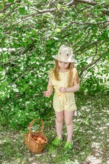 Joyful little girl in a cute yellow outfit happily picking fresh apples in a vibrant green garden.