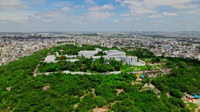 aerial view of falaknuma palace in the hill top with greenery, sky, clouds and crowded city buildings at engine bowli, falaknuma, hyderabad, telangana, india. day time, semi circle, drone shot, 4k.