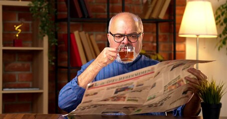 Indian senior retired man wears kurta, reads morning newspaper while sipping black coffee at home desk, staying updated on current business affairs and feeling relaxed