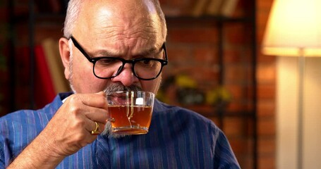 Indian senior retired man uses smartphone to read or browse the internet while sipping black coffee at home desk, looking relaxed and staying updated on current affairs