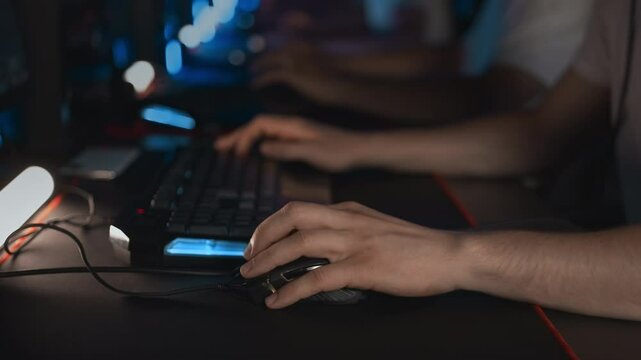 Gamer plays video game on PC at computer club with team. Skill. E-sport tournament Professional cyber sport championship. Focus on gaming mouse RGB light keyboard on mat. Multiplayer shooter strategy