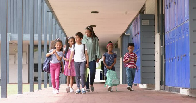Walking in school hallway, teacher and diverse group of students with backpacks