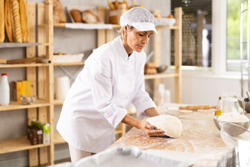 Working in bakery - woman kneads raw dough to make baguettes or croissants