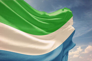 Waving flag of Sierra Leone in blue sky. Sierra Leone flag on pole for Independence Day. The symbol of the state on wavy fabric.