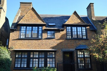 Fototapeta premium Historic brick house with large windows and a well-maintained garden situated in a quiet neighborhood under bright blue skies