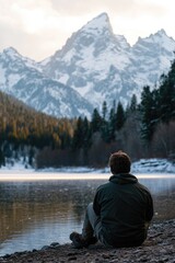 A person sitting on the edge of a serene mountain lake, surrounded by nature