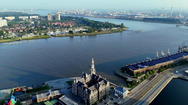 Drone footage of Antwerp Belgium showcasing historic city blending with industrial port along the Scheldt River under a clear morning sky, with prominent landmarks like the Het Steen castle visible