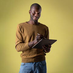 Smiling African man using a digital tablet with stylus on yellow background
