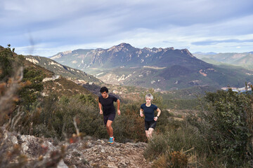 Man and woman trail running uphill with scenic mountain landscape in the background