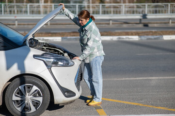 Naklejka premium Caucasian woman looks puzzled under the hood of a car. 