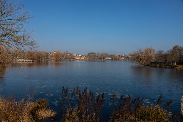 Scenic view of a calm lake surrounded by trees and buildings during a clear day in early autumn