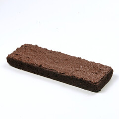A rich chocolate brownie with a smooth chocolate frosting rests on a plain white surface, highlighting its decadent layers