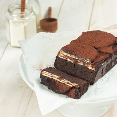 Delicious chocolate layered cake with creamy filling is showcased on a white cake stand in a cozy baking setting, complete with ingredients nearby