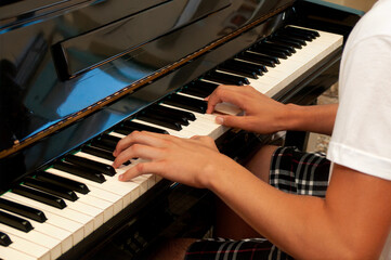 Fototapeta premium Close-up of a young person playing piano, showcasing hands and keys in an indoor setting 