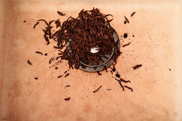Wet tea leaves in metal sink drain with beige surface. Scattered tea particles create a messy...