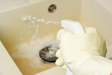 A hand in a rubber glove sprays an alkaline cleaning solution onto a dirty kitchen sink. Foam...