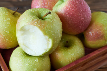 Fresh apples with drops of water in a wooden box.  Overbitten apple. Selective focus.