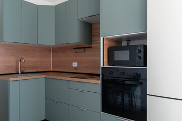 Modern built-in kitchen in minimalist style. Interior of contemporary kitchen with comfortable. blue kitchen unit, wooden countertop and kitchen backsplash. built-in oven and microwave. 