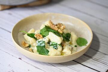 Close-up view of homemade potato gnocchi being prepared in the kitchen, with a creamy cheese sauce and fresh spinach leaves being added. 