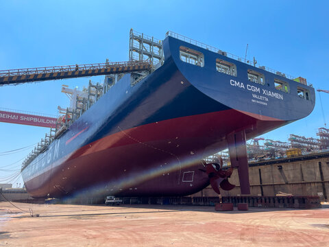 10.08.2024 - Qingdao, China. Large container ship CMA CGM XIAMEN in dry dock with stern, hull, and propeller visible during maintenance.