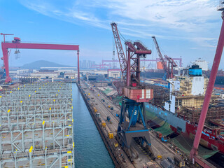 Wide view of containers ship inside the shipyard with cranes, vessels, and dock facilities under...