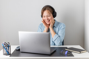 Success, victory or meeting deadline concept. Smiling excited caucasian woman freelancer with headphones behind a laptop is holding her hands up in the air. Success concept