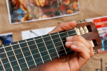 A close-up shows a person's hand gently strumming the strings of a guitar. The fretboard is dark,...