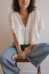 Woman in White Blouse and Loose Jeans Sitting Cross-Legged on Stool. Minimalist Aesthetic Fashion...