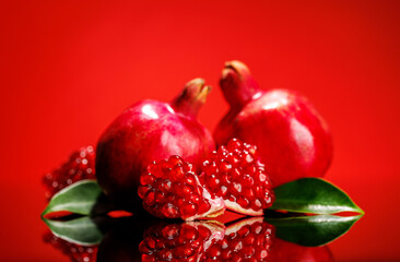 A ripe, glossy pomegranate placed against a vibrant red background
