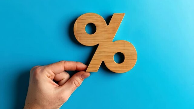 Wood percentage sign in a human hand. Blue studio background, copy space. Symbol percent. Seasonal sale, discount. Rate for finance, return. Investment ROI, credit, mortgage, tax, marketing, promotion