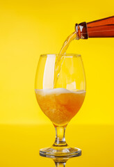 A frothy glass of fresh beer against a bright yellow background